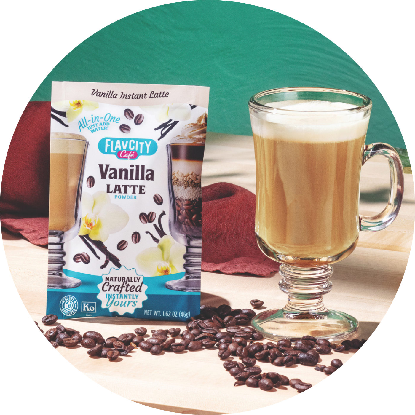 A glass mug of vanilla latte sits beside a pouch of FlavCity Café Vanilla Latte powder on a wooden surface, with coffee beans scattered around and a red cloth in the background.