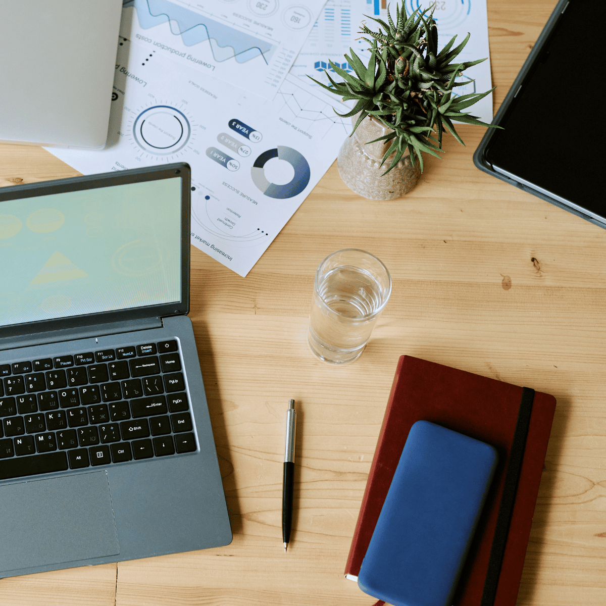 A desk with a laptop, pen, wallet and a glass of water.