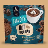 A pouch of FlavCity Hot Chocolate Mix in Single-Serve Packets featuring a cup of cocoa with marshmallows, chocolate chunks, and cocoa powder, with text highlighting 5g of protein and fiber per serving.