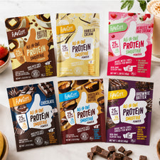 Six packets of Shop FlavCity All-In-One Protein Smoothie Packets—featuring grass-fed whey protein in flavors like Butter Coffee, Vanilla Cream, Berries & Cream, Chocolate, Peanut Butter Chocolate, and Brownie Batter—are displayed on a light surface.