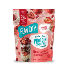 A pouch of Shop FlavCity Berries & Cream Protein Smoothie powder next to a glass filled with the mix, surrounded by splashing milk, fresh strawberries, and collagen.