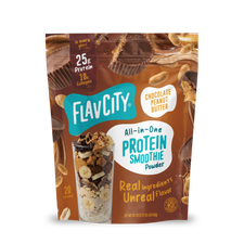 A stand-up pouch of Shop FlavCity Chocolate Peanut Butter Protein Smoothie powder next to a glass filled with a smoothie topped with banana slices, nuts, and chocolate shavings.