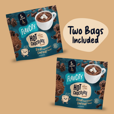 Two square packets of Shop FlavCity Hot Chocolate Mix in Single-Serve Packets, each featuring a mug with marshmallows and the text Real Ingredients, Unreal Flavor, with a graphic indicating two bags included.