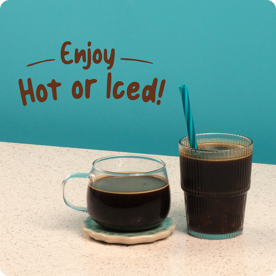 Two glasses of Coffee With Benefits Medium Roast by Shop FlavCity, one served hot in a clear mug and the other iced in a ribbed glass with a blue straw, sit on the counter. “Enjoy Hot or Iced!” is written on the blue background above them.