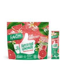 A package and stick pack of Shop FlavCity Grapefruit Lemonade, a healthy drink shown with sliced grapefruits, flowers, and leaves on a pink-green background. Text highlights vitamin C, easy mixing, and sugar-free ingredients.