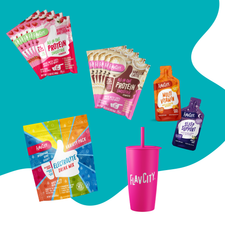 The Shop FlavCity Travel Kit, featuring protein smoothie packets, electrolyte drink mix, multivitamin, sleep support packs, and a bright pink tumbler with straw, displayed on a blue and white background.