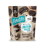 A bag of Shop FlavCity Cookies & Cream Protein Smoothie, made with grass-fed whey and 10g collagen, is pictured next to tasty cookies and a creamy smoothie. The packaging showcases 25g of protein per serving from real ingredients, with each bag providing 20 servings.