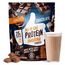 A package of Shop FlavCity Chocolate Protein Smoothie sits behind a glass of chocolate smoothie and chocolate pieces, emphasizing 25g collagen protein, 10g collagen, grass-fed whey, and natural ingredients on its packaging.
