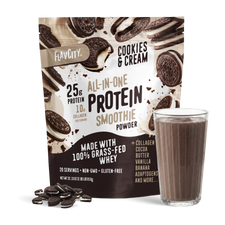 A bag of Shop FlavCity Cookies & Cream Protein Smoothie stands behind a glass of chocolate smoothie and some cookies scattered on a white surface.