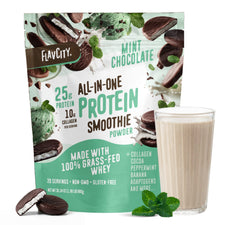 A bag of Shop FlavCity’s Mint Chocolate Protein Smoothie stands behind a glass of smoothie, with packaging featuring 25g protein and 10g collagen per serving. Mint leaves and chocolate pieces decorate the scene.