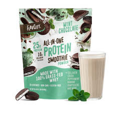 A pouch of Shop FlavCity Mint Chocolate Protein Smoothie stands behind a filled glass, with mint leaves and chocolate pieces nearby on a white background.