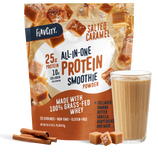 A bag of Shop FlavCity Salted Caramel Protein Smoothie stands behind a glass of the creamy salted caramel drink. Cinnamon sticks and caramel pieces are placed nearby, while the packaging showcases its protein, collagen, and featured ingredients.