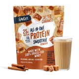 A bag of Shop FlavCity Salted Caramel Protein Smoothie stands behind a glass of the creamy salted caramel drink. Cinnamon sticks and caramel pieces are placed nearby, while the packaging showcases its protein, collagen, and featured ingredients.