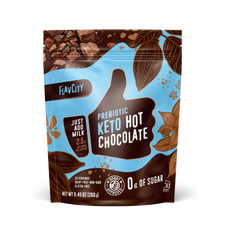 FlavCity Prebiotic Keto Hot Chocolate mix in a resealable blue and brown bag. The design features a white thumb-up graphic and text promoting 'Just add milk,' '2.5g net carbs,' '0g of sugar,' and 'Bobby Approved,' with illustrations of cocoa beans, leaves, and chocolate chunks.