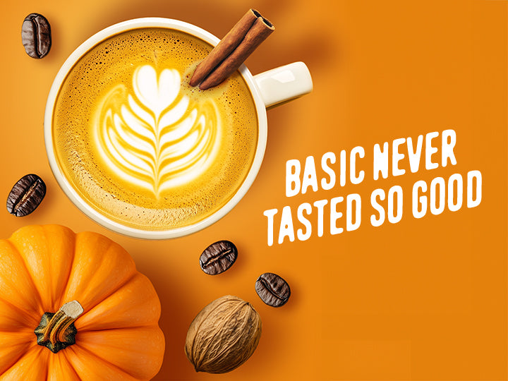 Cup of pumpkin spice latte with latte art, pumpkins, and nuts on an orange background with text 'Basic never tasted so good'.