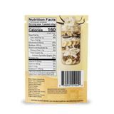 A packet of Shop FlavCity Vanilla Cream Protein Smoothie features a clear window displaying the granola, banana chips, and nuts inside. The back shows the Nutrition Facts label and barcode, while the top of the package is decorated with white flowers and antler graphics.
