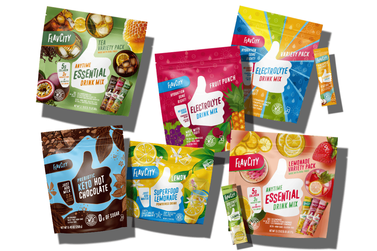 Six colorful FlavCity drink mix packages, including Essential, Electrolyte, Keto Hot Chocolate, and Superfood Lemonade, are arranged with individual stick packs displayed beside and in front of the bags.