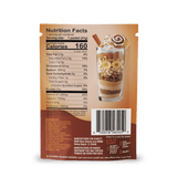 Back of a Shop FlavCity Protein Smoothie Single-Serve Cinnamon Roll packet with nutrition facts, ingredients, and barcode; above is a glass dessert layered with whipped cream, banana slices, wafers, and a rolled wafer garnish.