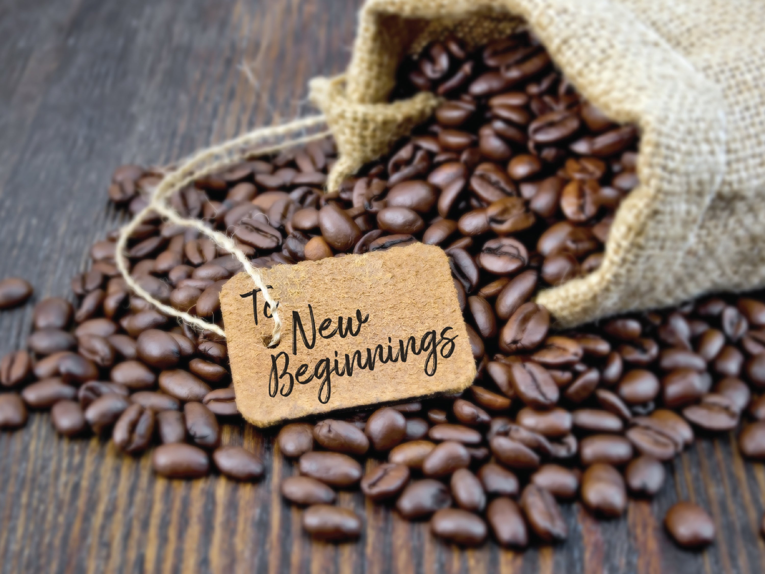 Coffee beans with a bag and 'New Beginnings' tag on a wooden surface