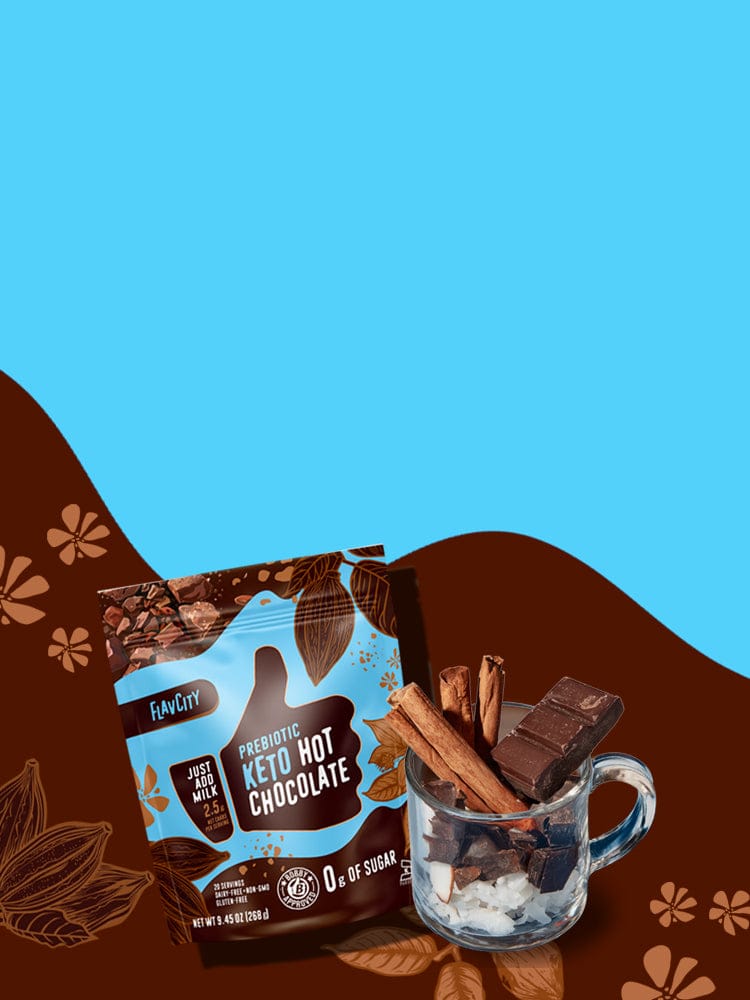 A package of FlavCity Prebiotic Keto Hot Chocolate is displayed next to a glass mug filled with whipped cream, chocolate pieces, and cinnamon sticks, set against a blue and brown floral background.